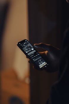 Close-up of a hand holding a smartphone displaying a dark app interface.